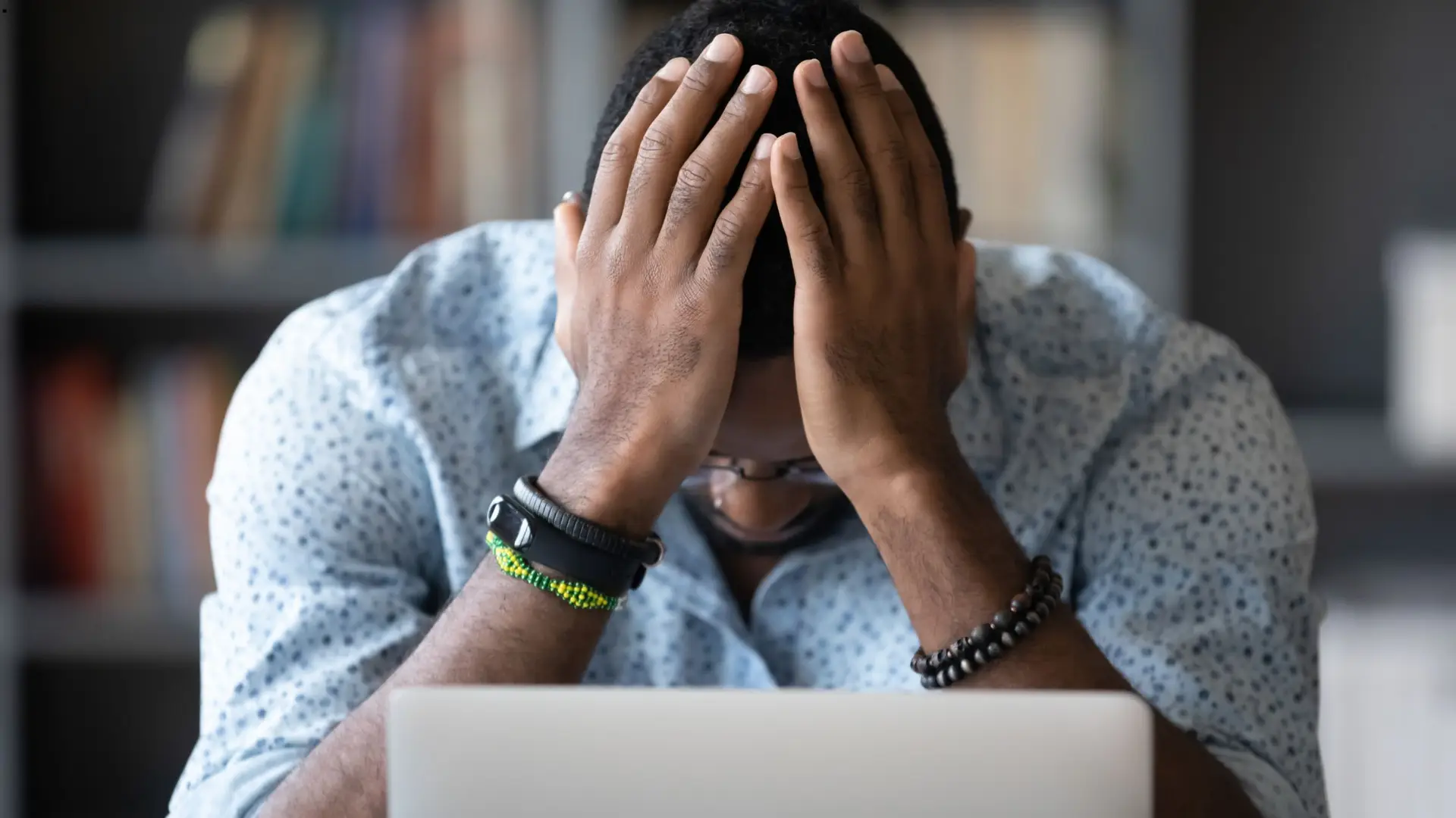 Image if a young man with his hands on his head in frustration sitting in front of a laptop computer. The image represents why Soulheart left Google Analytics because of our frustrations with GA4 and moved to Fathom Analytics.