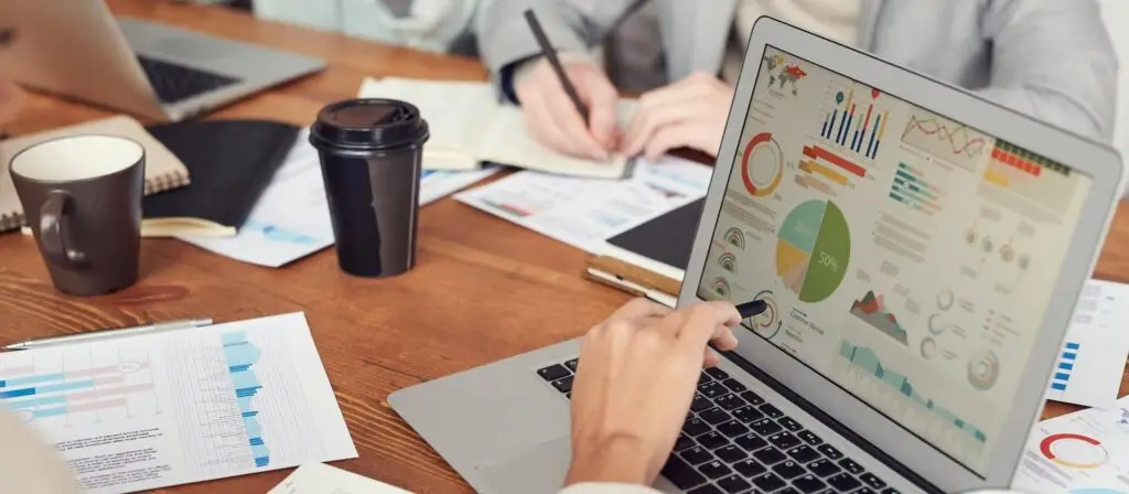 An image of a team looking at a laptop with charts and graphs on it representing Soulheart's blog titled Content Excellence: 5 Benefits of Working with Digital Marketers.